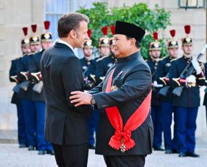 Presiden Republik Indonesia Prabowo Subianto mengenakan pakaian formal lengkap dengan selendang merah bintang penghargaan Grand Croix de la Légion d'Honneur, tampak tersenyum hangat saat berjabat tangan dengan Presiden Prancis Emmanuel Macron di dalam ruang megah Salle des Fêtes, Istana Élysée.