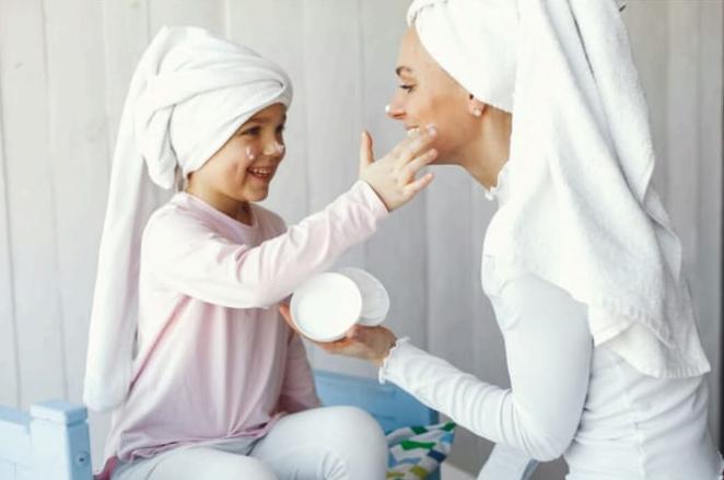 Seorang ibu sedang mengoleskan krim pelembap bayi secara lembut pada area wajah anaknya untuk mencegah iritasi kulit kering.