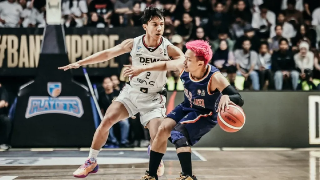 Andakara Prastawa melakukan manuver lay-up melewati penjagaan ketat Joshua Ibarra di dalam area paint Dewa United Arena.